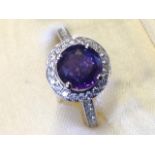 An 18ct gold sapphire & diamond halo ring, the claw set circular purple sapphire of nearly two