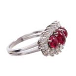 Ruby and diamond cocktail ring with three oval cabochon rubies surrounded by a border of sixteen