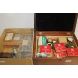 Two boxes containing a selection of clock and watchmaking equipment, parts, screws,