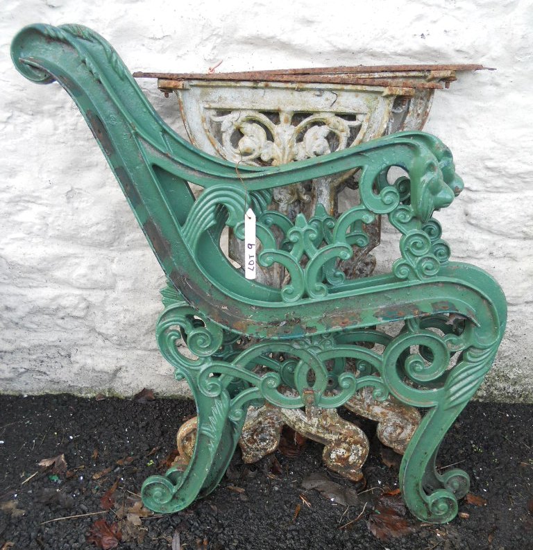 A pair of painted iron bench ends with lion mask scroll arms - sold with a pair of older cast iron