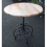 A stripped wood circular table set on an ornate wrought iron stand