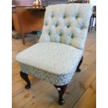 A reproduction button back nursing chair with green floral upholstery, set on polished wood cabriole