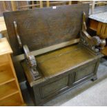 A 20th Century carved oak monk's bench with flanking lion pattern arm rests and locker seat