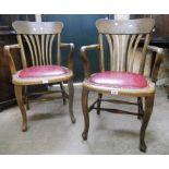 A pair of early 20th Century oak framed office elbow chairs, with lathe backs and studded red