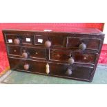 A 21" antique mahogany and mixed wood tabletop chest with an array of six drawers of varying size
