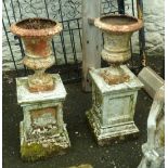 A pair of 16" Victorian cast iron urns, set on 19" terracotta pedestals