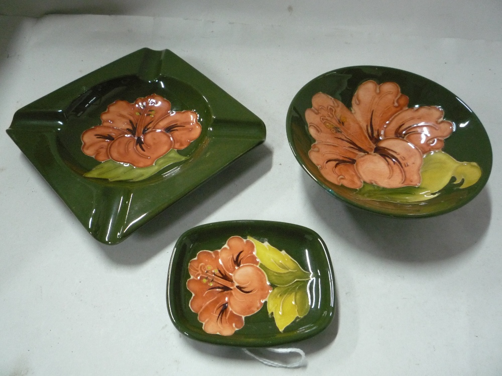 THREE PIECES OF MOORCROFT POTTERY 'HIBISCUS' PATTERN, to include ashtray and two pin trays,
