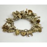A CHARM BRACELET, comprising of thirty white metal novelty charms to the heart shape padlock