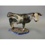 A 19TH CENTURY COW CREAMER, with black and grey sponge decoration, set on pink, green, black and