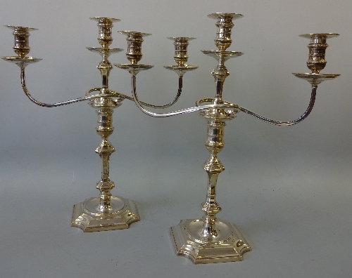 A PAIR OF SILVER THREE BRANCH CANDELABRA, on shaped square bases with central urn supports flanked