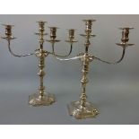 A PAIR OF SILVER THREE BRANCH CANDELABRA, on shaped square bases with central urn supports flanked