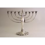 A SILVER MENORAH, with filled scalloped base, tapering central support with graduating arms and