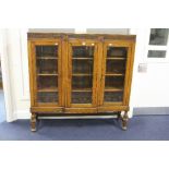 A CARVED OAK BREAKFRONT GLAZED TRIPLE DOOR BOOKCASE, with fielded panelled sides, approximate size