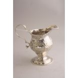 A SILBER MILK JUG, of urn form with repousse floral and leaf decoration, vacant cartouches, beaded