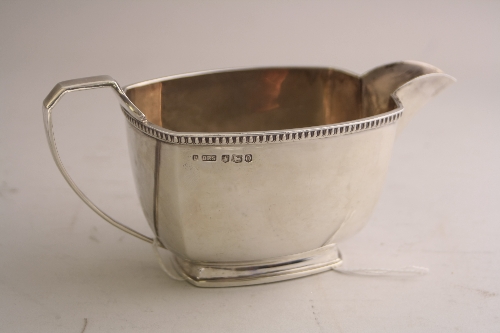 A SILVER MILK JUG, of shaped rectangular form on foot, shell thumb rest to loop handle, Sheffield