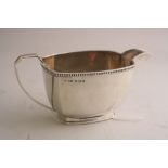 A SILVER MILK JUG, of shaped rectangular form on foot, shell thumb rest to loop handle, Sheffield