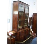 A REGENCY GLAZED TWO DOOR BOOKCASE, with two internal drawers to upper section and cupboard base,