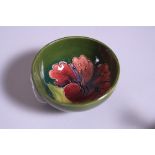 A SMALL MOORCROFT POTTERY FOOTED BOWL, Hibiscus pattern on green ground, impressed marks to base,