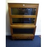 AN OAK GLAZED THREE SECTION BOOKCASE, with lower drawer, Gumm label attached to lower section,