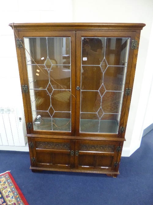 AN 'OLD CHARM' CARVED OAK LEAD GLAZED TWO DOOR DISPLAY CABINET, with solid cupboard below,