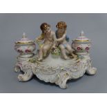 A SITZENDORF DESK TOP INKWELL, having figural seated cherubs flanked by floral decorated wells and