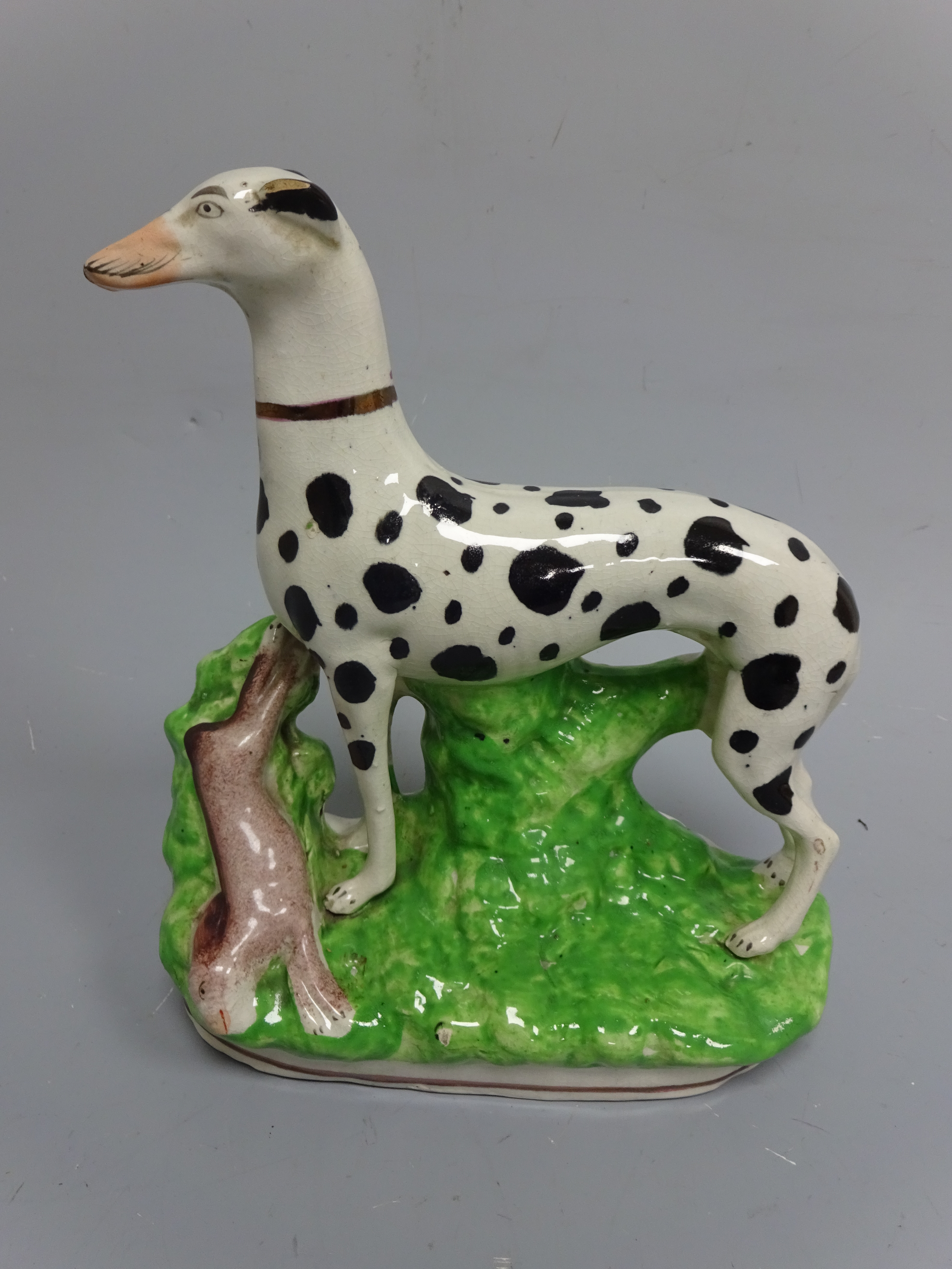 A STAFFORDSHIRE FIGURE, modelled as standing black and white spotted greyhound with dead hare, set