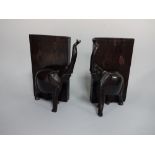 A PAIR OF CARVED EBONISED BOOKENDS, modelled as elephants with raised trunks before books,