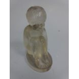 AN OPAQUE GLASS FIGURE, modelled as seated child with knees drawn in on oval plinth, approximately