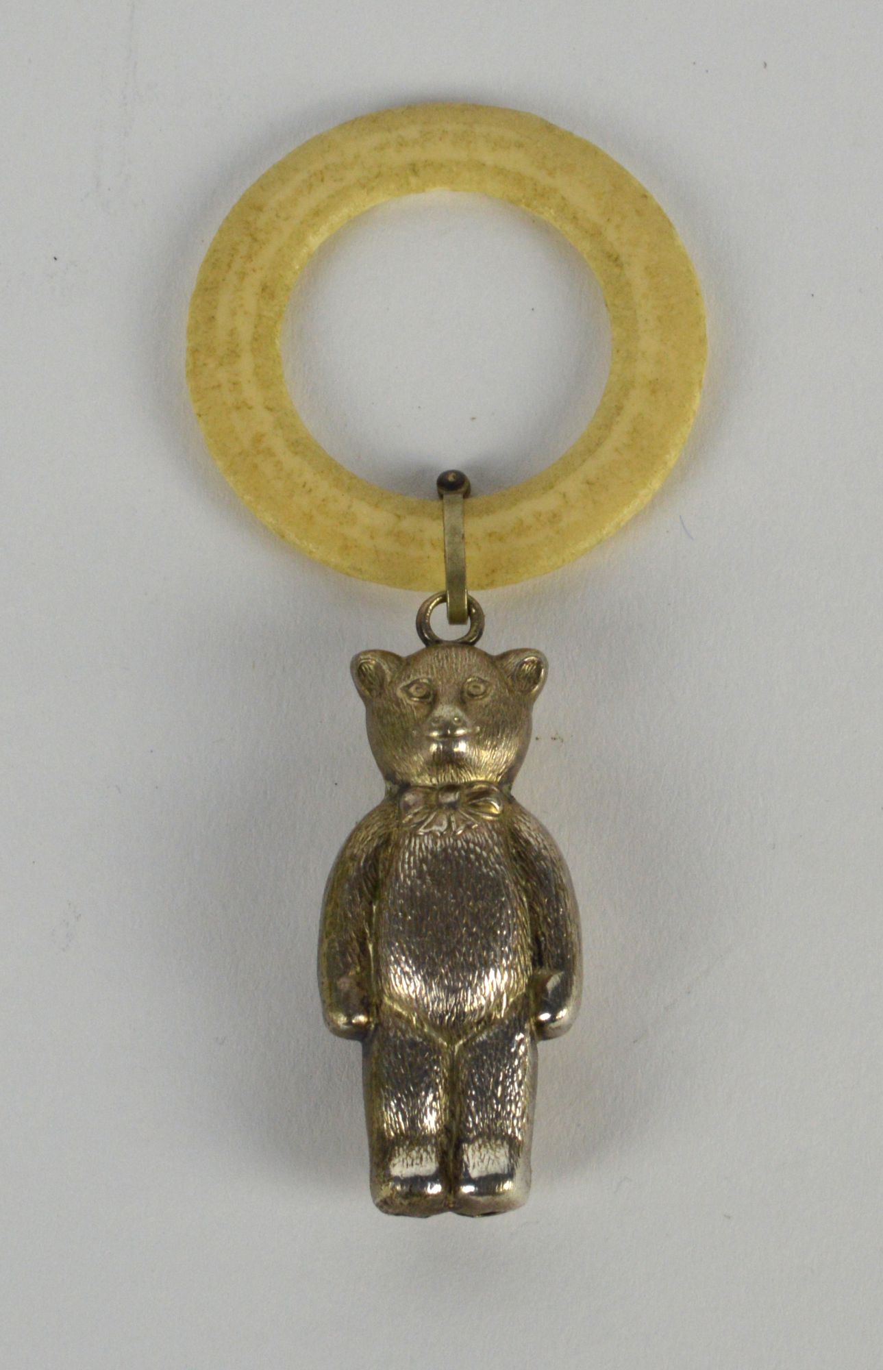 A silver plated babies teether, the ivory coloured plastic ring hung with a teddy bear.