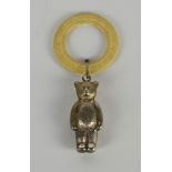 A silver plated babies teether, the ivory coloured plastic ring hung with a teddy bear.