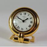 A Cartier circular gilt metal quartz travel clock, with folding stand, approx 8cm diameter,