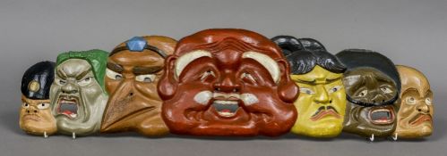 A Japanese painted carved wooden wall plaque Formed as various theatrical masks. 90 cm wide.