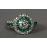 A diamond and emerald set white metal target ring The central stone approximately 0.50 carat.