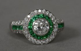 A diamond and emerald set white metal target ring The central stone approximately 0.50 carat.