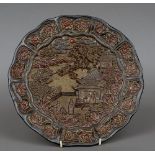 A Chinese lacquered plate Worked with figures and pagodas in a river landscape within floral carved