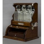 A late Victorian white metal mounted oak three bottle tantalus The decanters housed above a rising