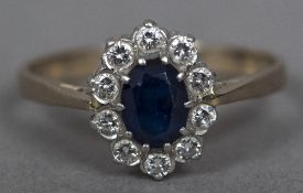 An 18 ct gold diamond and sapphire cluster ring The central facet cut sapphire flanked by a row of