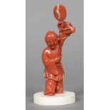 A Chinese carved coral group Worked as a young boy holding aloft a fan,