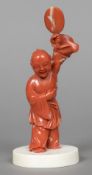 A Chinese carved coral group Worked as a young boy holding aloft a fan,