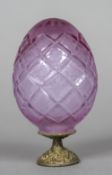 A Russian cut amethyst glass egg Lozenge cut and engraved with fruit, standing on a gilt metal base,