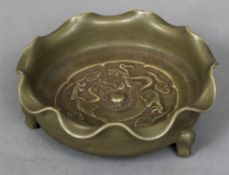 A Chinese porcelain dish Worked with a dragon within wavy rim, standing on tripod feet,