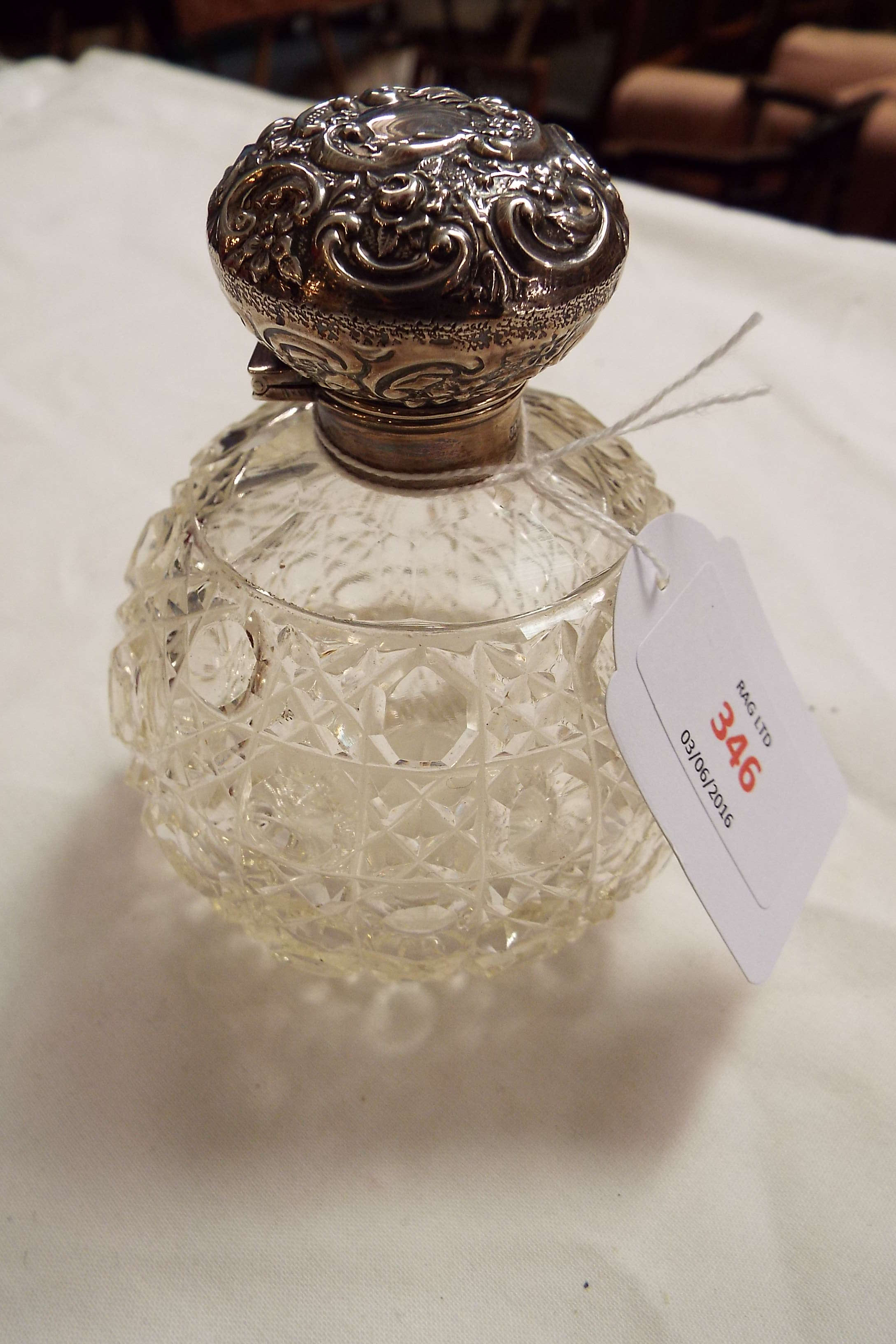 A Birmingham 1910 silver topped perfume bottle having embossed scroll decoration with hob-nail cut