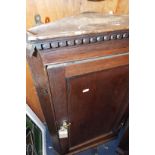 An early Victorian oak corner cabinet having brass 'H' hinges the panelled door enclosing two