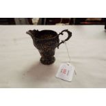 A German 800 silver miniature cream jug having embossed scroll and floral decoration