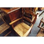 An oak open armchair the ladder-back carved with shield motif over a rush upholstered seat