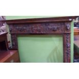 Stained pine fire surround with carved detail with central panel depicting cherubs with lion masks