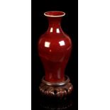 A small Chinese flambe glazed baluster vase, 6.8ins. (17.3cms.) high, on associated carved