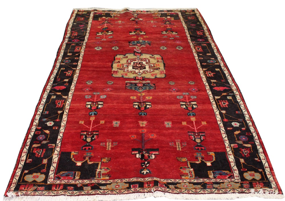 A Kordi woollen hand-made rug with red ground, 116 by 66ins. (295 by 170cms.) (see illustration).