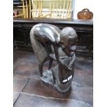 Carved African Hardwood Figure Group, featuring squatting gentleman with another bent over in