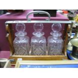 An Early XX Century Oak Cased Three Bottle Tantalus, lead cut crystal whisky decanters (chips